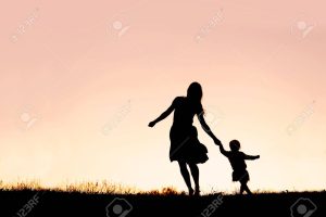 Silhouette of a happy mother and her baby daughter holding hands, and running and dancing outside at sunset.